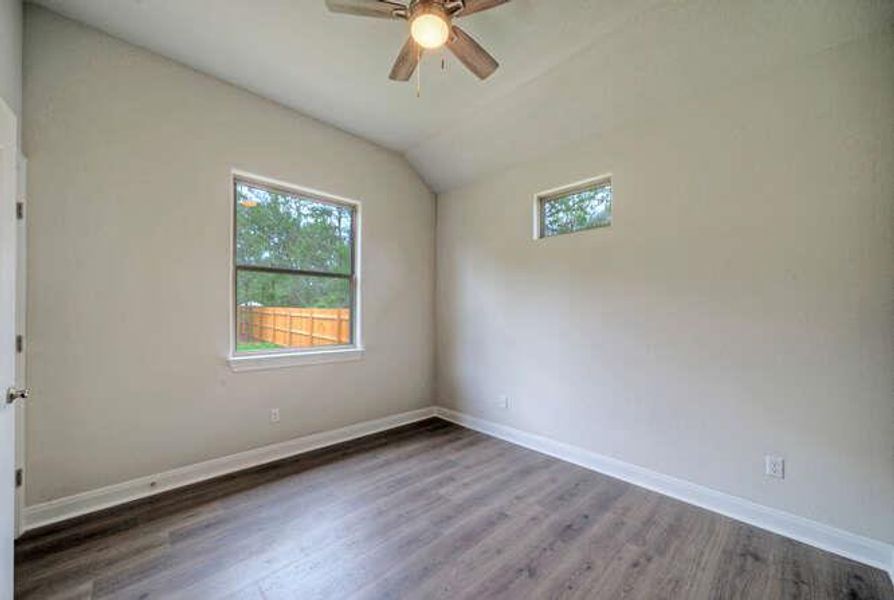 Empty room with a ceiling fan, wood finished floors, and lofted ceiling