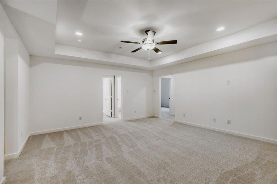 Spacious room featuring neutral carpeting, white walls, a tray ceiling with a ceiling fan, recessed lighting, and white baseboards