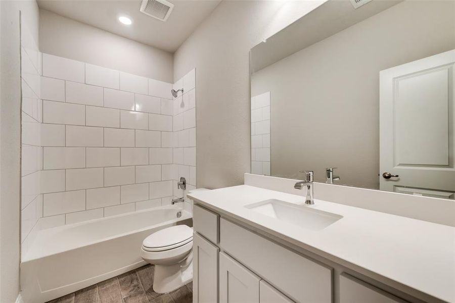 Full bathroom with tiled shower / bath combo, vanity, hardwood / wood-style floors, and toilet