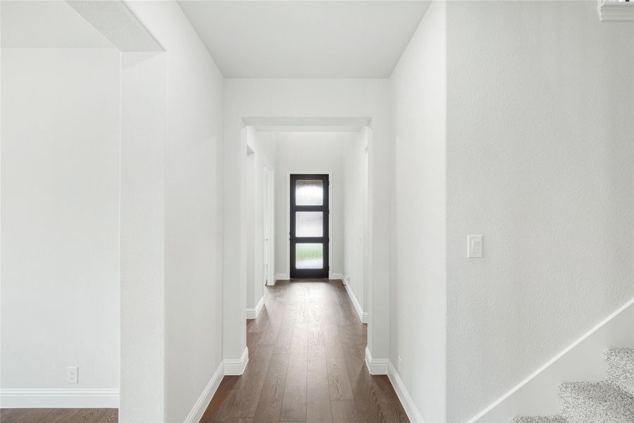 Hallway with white walls, dark hardwood floors, and black front door with glass panels at the end Hallway with white walls, dark hardwood floors, and black front door with glass panels at the end