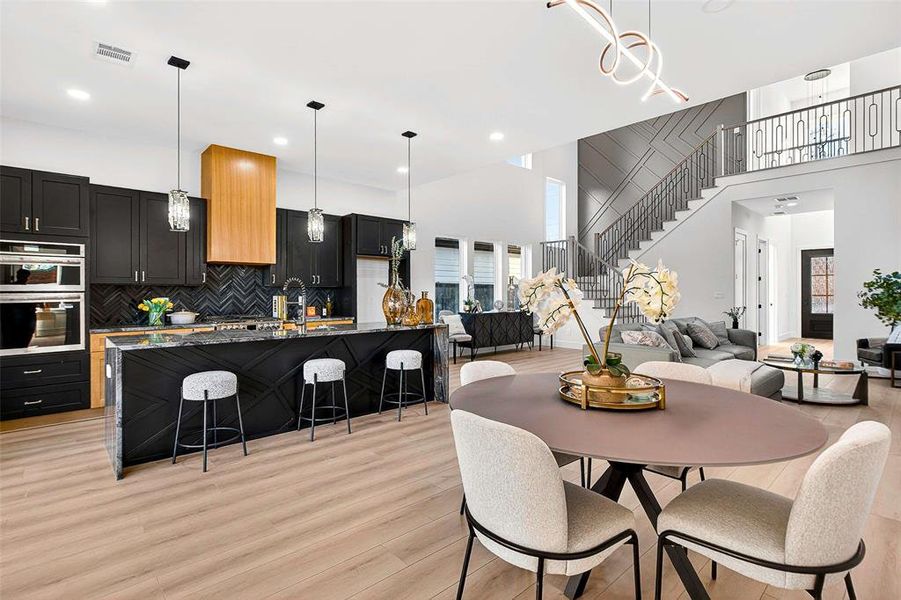 Dining space with stairs, a towering ceiling, light wood-type flooring, and a chandelier Dining space with stairs, a towering ceiling, light wood-type flooring, and a chandelier