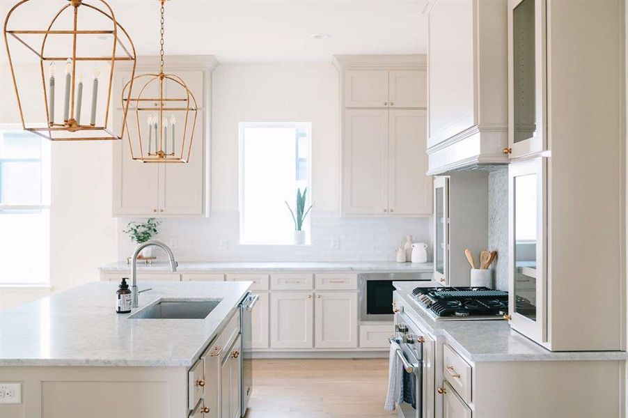 Kitchen with pendant lighting, sink, stainless steel stove, light stone countertops, and white cabinetry