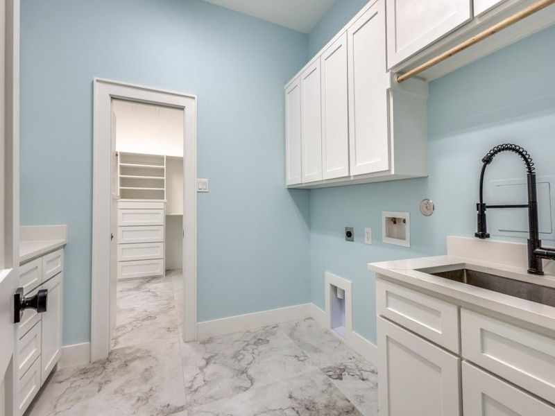 Washroom with cabinet space, light marble finish floors, electric dryer hookup, hookup for a washing machine, large sink with professional faucet, plenty of counter top and also a built in desk in between counters
