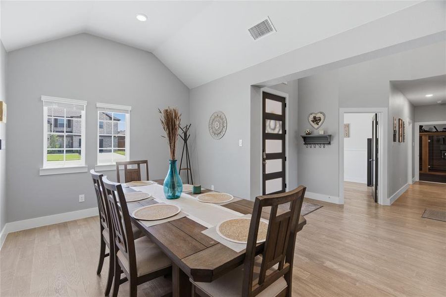 Dining area featuring light wood-finish flooring, vaulted ceiling, and two large windows