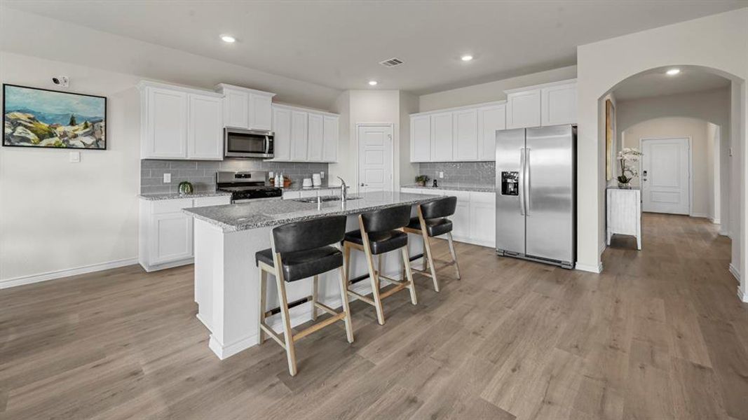 Kitchen featuring white cabinetry, arched walkways, appliances with stainless steel finishes, backsplash, and a kitchen bar