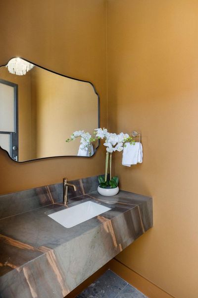 A stylish bathroom features a striking marble vanity, a sleek modern mirror, and warm mustard-yellow walls.