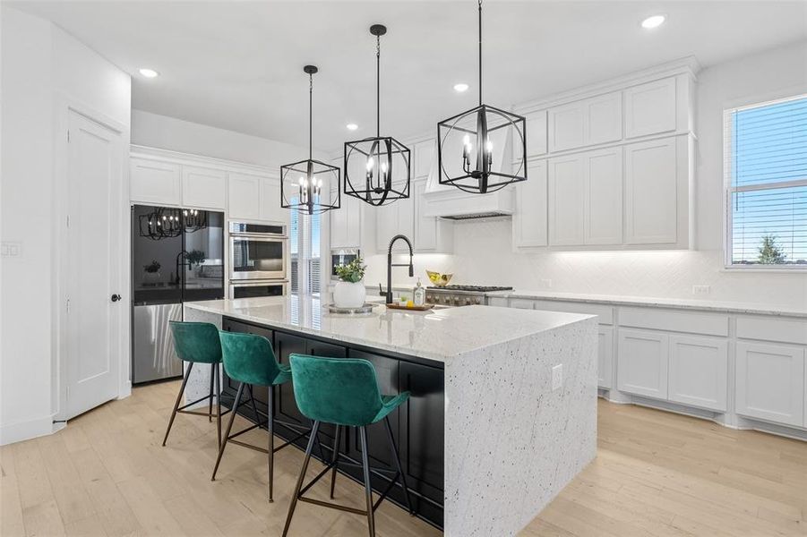 Kitchen featuring decorative light fixtures, white cabinets, stainless steel appliances, light wood-type flooring, and light stone counters Kitchen featuring decorative light fixtures, white cabinets, stainless steel appliances, light wood-type flooring, and light stone counters