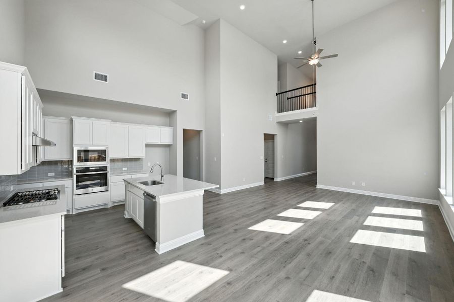 Kitchen featuring white cabinets, a center island with sink, backsplash, appliances with stainless steel finishes, and a high ceiling Kitchen featuring white cabinets, a center island with sink, backsplash, appliances with stainless steel finishes, and a high ceiling