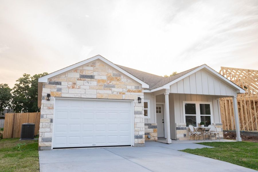 View of front of house featuring stone siding, concrete driveway, board and batten siding, an attached garage, and central AC unit