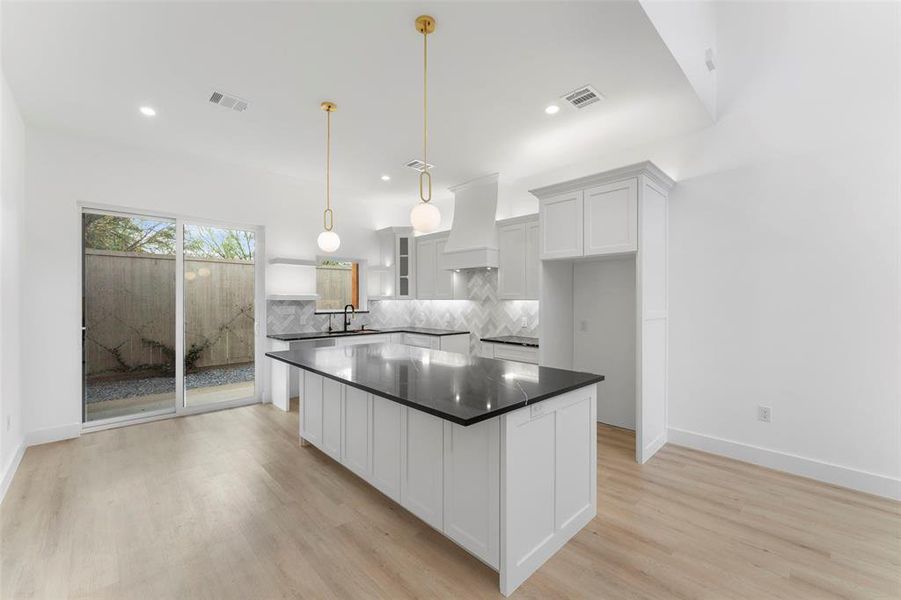 Kitchen with white cabinets, decorative backsplash, a kitchen island, glass insert cabinets, and decorative light fixtures