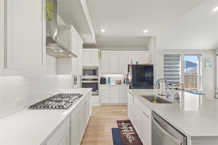 Kitchen featuring white cabinets, light wood finished floors, light stone counters, appliances with stainless steel finishes, and recessed lighting