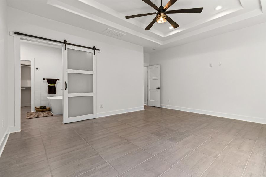 Empty room featuring a barn door, a raised ceiling, recessed lighting, and a ceiling fan