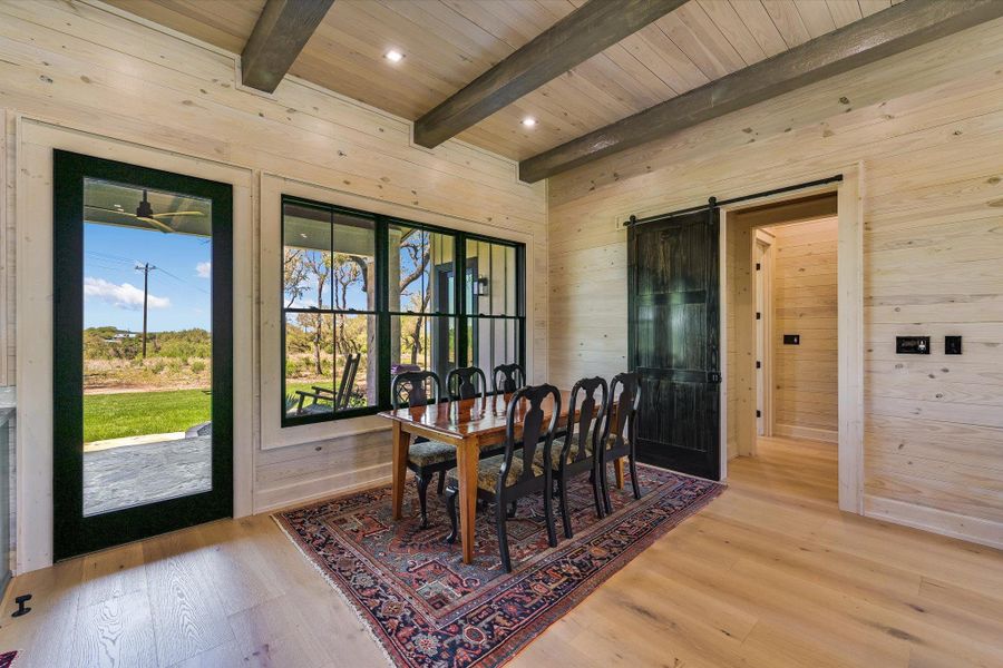 Dining space featuring a barn door, light wood-style flooring, wood walls, recessed lighting, and a wooden ceiling with exposed beams