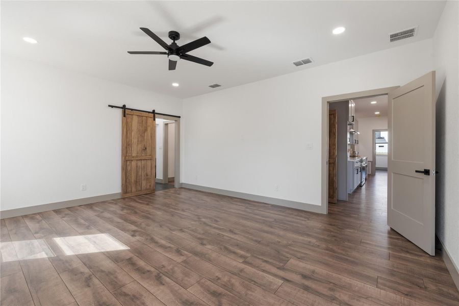 Empty room featuring a barn door, wood finished floors, a ceiling fan, and visible vents