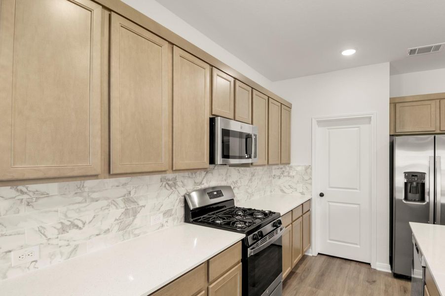 Kitchen with appliances with stainless steel finishes, decorative backsplash, light wood-style flooring, light brown cabinets, and light stone countertops Kitchen with appliances with stainless steel finishes, decorative backsplash, light wood-style flooring, light brown cabinets, and light stone countertops