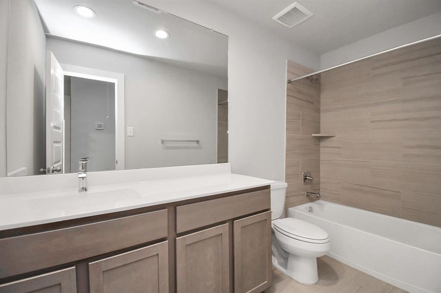 Secondary bathroom, where the tile flooring harmonizes with a bath/shower combo surrounded by tasteful tile. Light wood cabinets, coupled with a gorgeous countertop, elevate the space, cultivating a truly welcoming atmosphere. Sample photo of completed home. Actual colors and selections may vary.