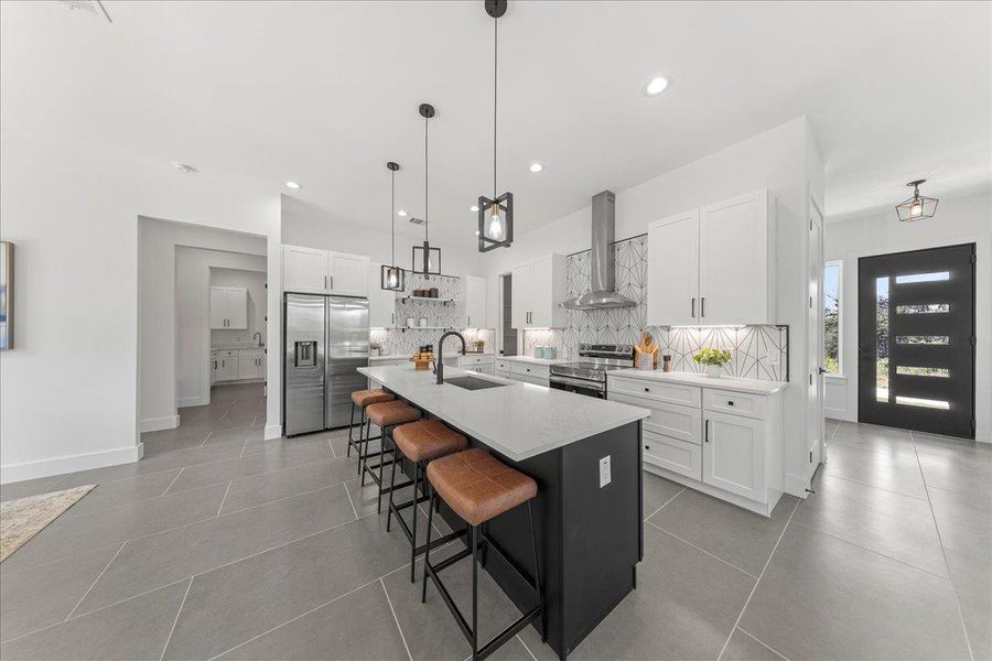 Kitchen featuring wall chimney exhaust hood, appliances with stainless steel finishes, decorative backsplash, a kitchen bar, and white cabinets Kitchen featuring wall chimney exhaust hood, appliances with stainless steel finishes, decorative backsplash, a kitchen bar, and white cabinets