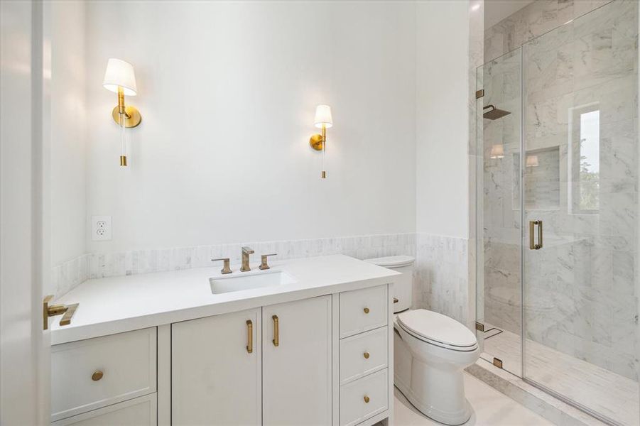 This elegant ensuite bathroom features a walk-in shower with stunning marble floor and wall tile, creating a luxurious retreat. Quartz countertops, designer brass sconces, and a custom vanity with ample storage combine both style and functionality in this beautifully designed space.