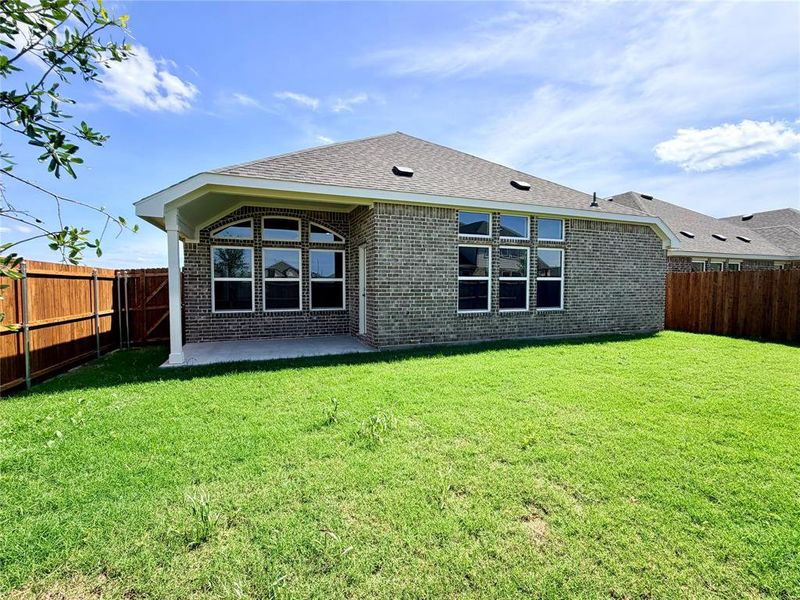 Spacious backyard featuring a covered patio, brick exterior, multiple windows, and privacy fencing