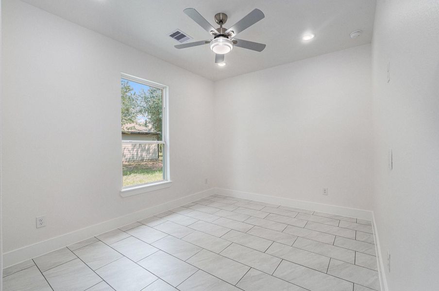 This bright room features large tile flooring, a ceiling fan with lights, and a window providing natural light and a view of the yard. The neutral walls enhance the spacious feel, making it a versatile space for any purpose. This bright room features large tile flooring, a ceiling fan with lights, and a window providing natural light and a view of the yard. The neutral walls enhance the spacious feel, making it a versatile space for any purpose.