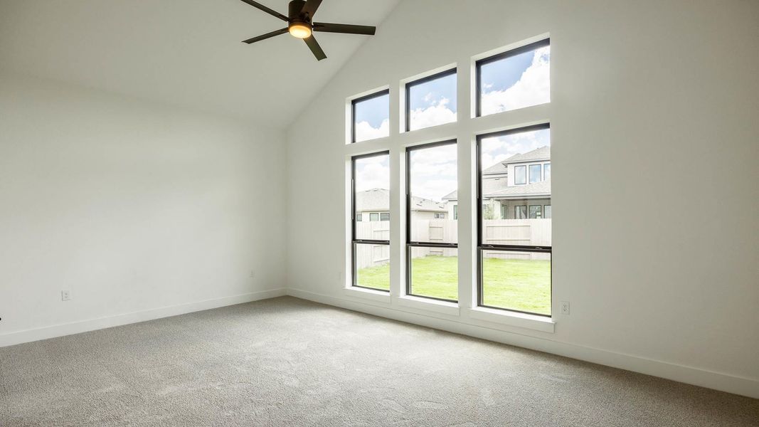 Empty room with high vaulted ceiling, light colored carpet, and a ceiling fan Empty room with high vaulted ceiling, light colored carpet, and a ceiling fan