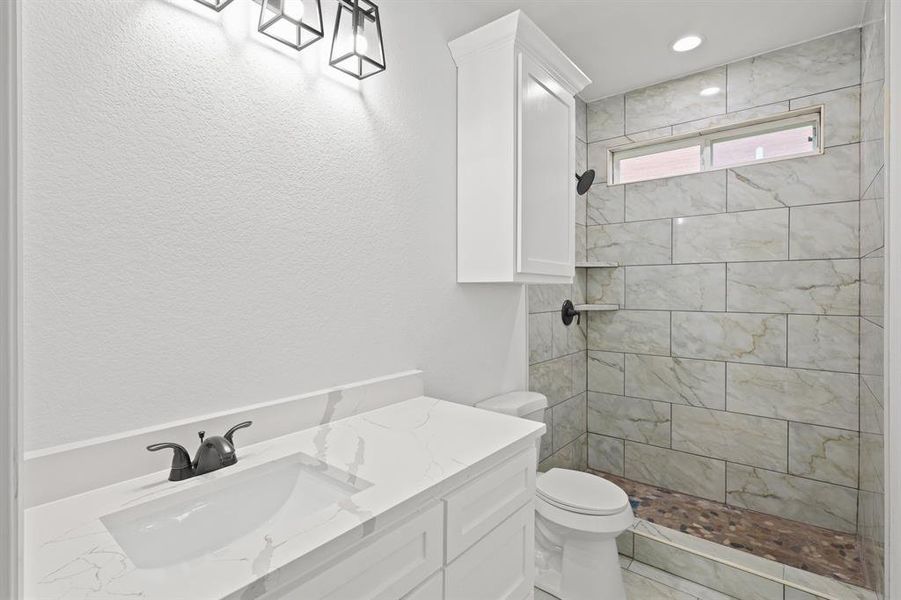 Bathroom featuring a tile shower, vanity, and toilet