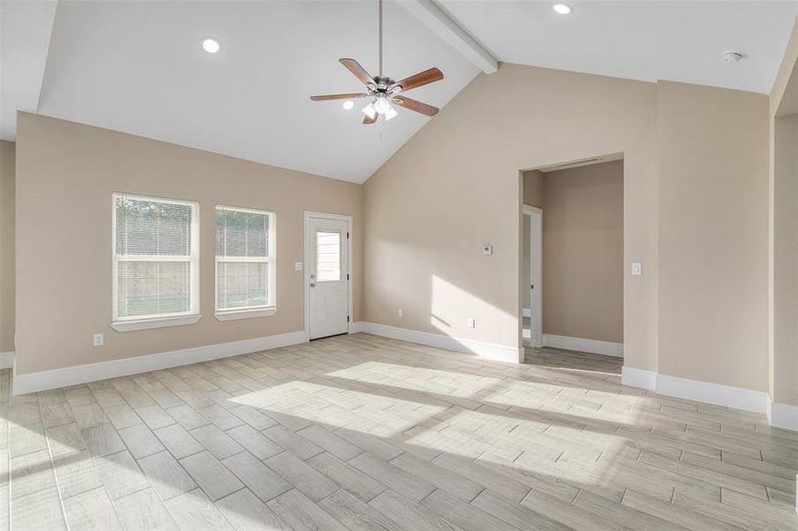 Unfurnished living room with beam ceiling, high vaulted ceiling, light hardwood / wood-style flooring, and ceiling fan