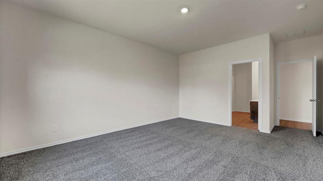 Spacious room featuring neutral tone carpeting and walls, recessed lighting, and white baseboards