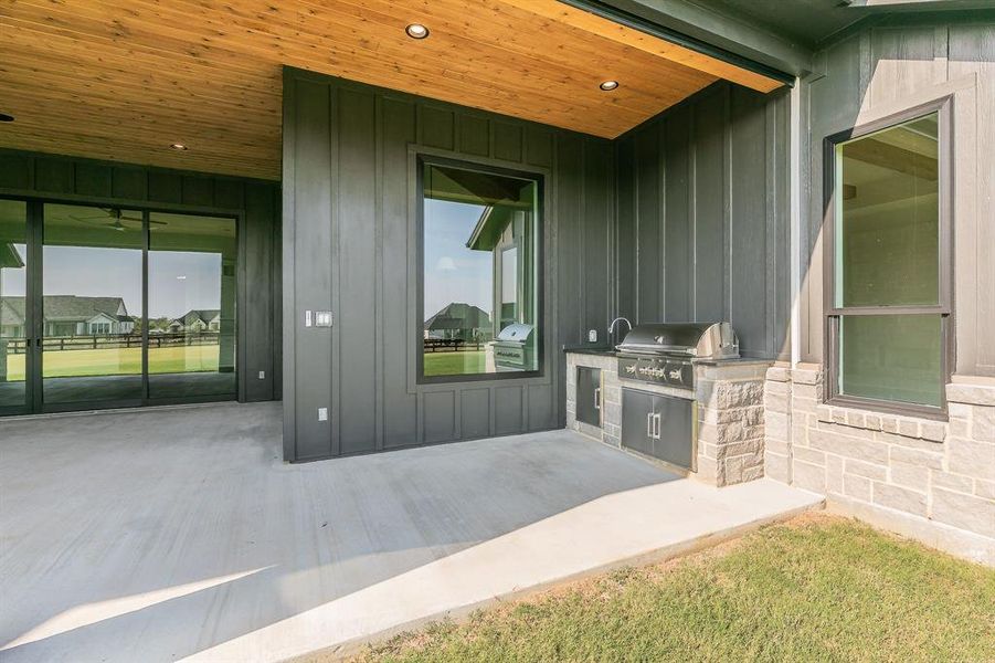 Property entrance with board and batten siding, area for grilling, a patio, and stone siding