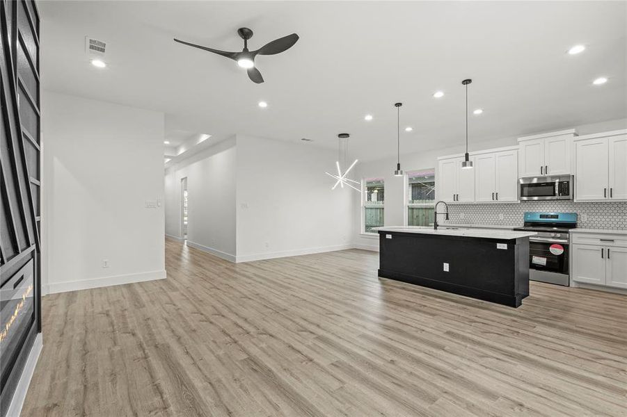 Kitchen featuring stainless steel appliances, ceiling fan, decorative light fixtures, a center island with sink, and white cabinets