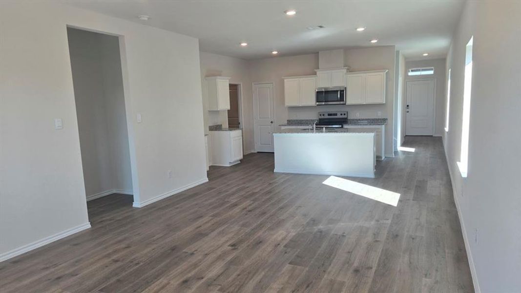 Kitchen with white cabinets, appliances with stainless steel finishes, an island with sink, dark wood finished floors, and open floor plan