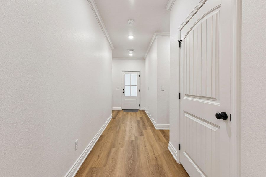 A well-lit hallway featuring elegant crown molding and rich hardwood flooring leading to an inviting glass-paneled door. A well-lit hallway featuring elegant crown molding and rich hardwood flooring leading to an inviting glass-paneled door.