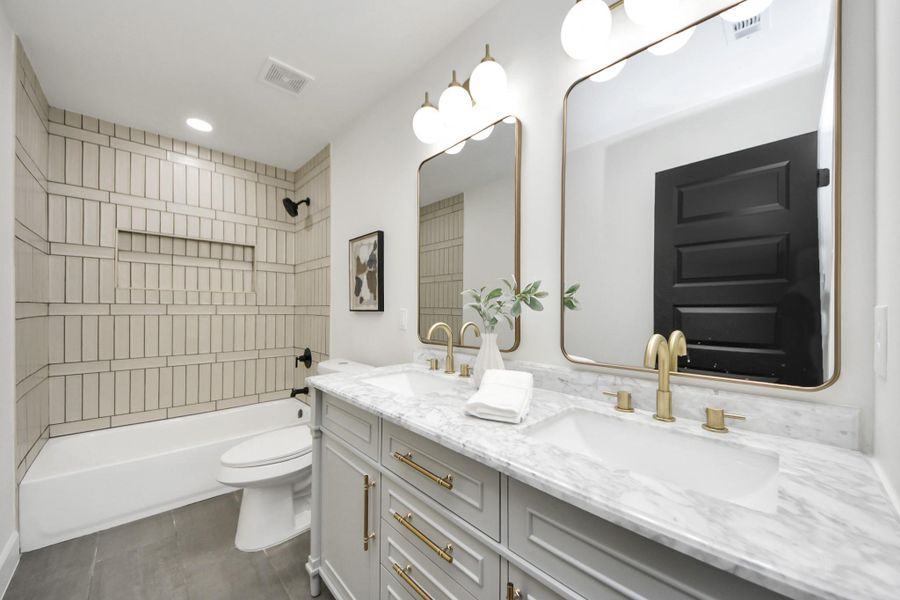 The secondary bathroom features a modern design with a dual-sink vanity, marble countertop, gold fixtures, and a contemporary tiled bathtub. Bright lighting and sleek mirrors enhance the spacious feel. The secondary bathroom features a modern design with a dual-sink vanity, marble countertop, gold fixtures, and a contemporary tiled bathtub. Bright lighting and sleek mirrors enhance the spacious feel.