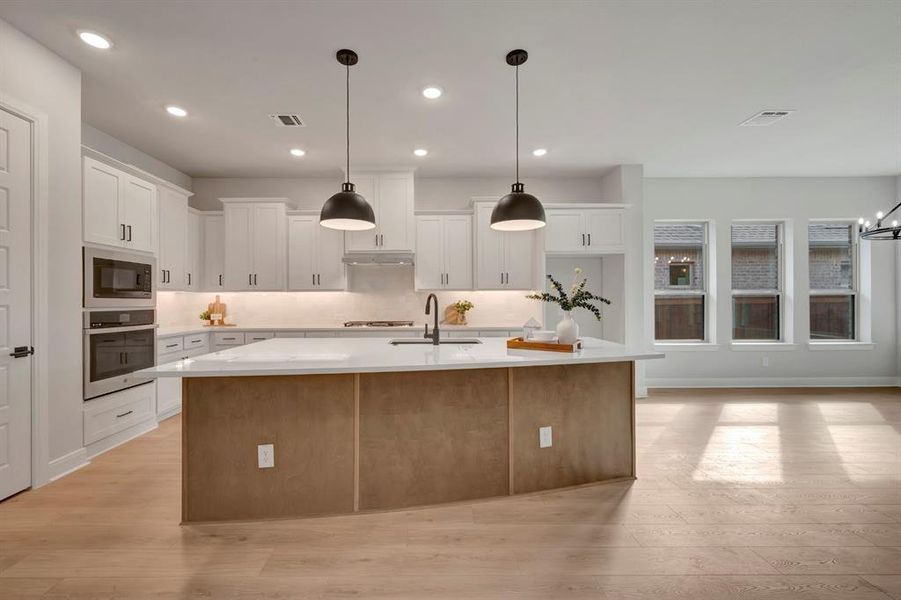 Two tone kitchen with a spacious island, light wood finished floors, stainless steel appliances, decorative light fixtures, and two tone cabinets