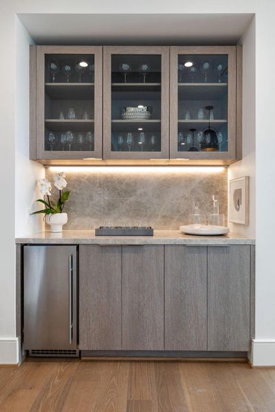 A built-in bar adds a touch of luxury to the space, featuring glass shelving for display and wine chiller.
