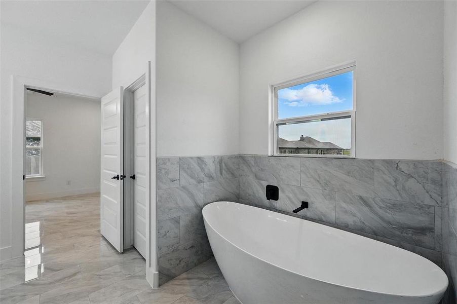 Bathroom featuring tile walls, marble tiled flooring, a freestanding bath, and wainscoting
