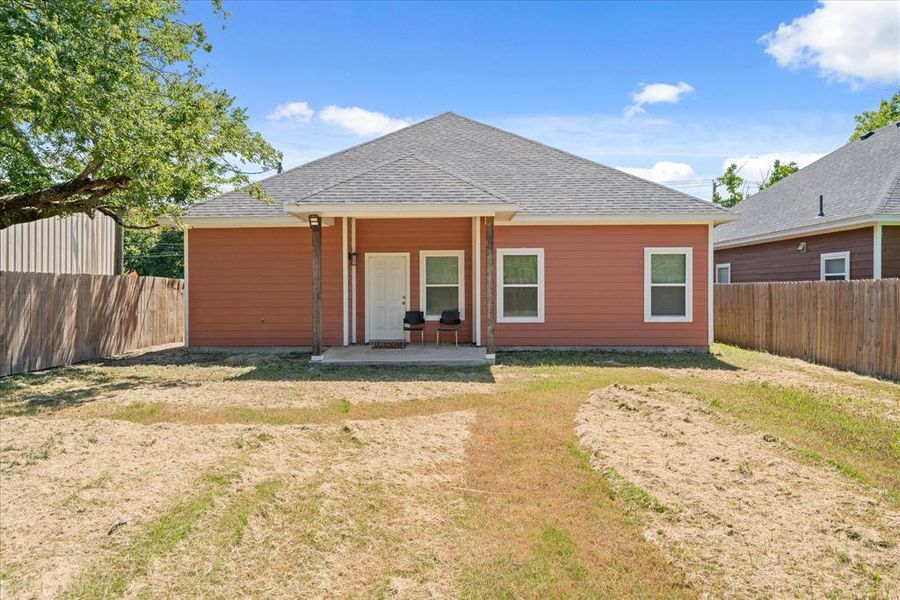 Rear view of property featuring a patio, a fenced backyard, and a shingled roof