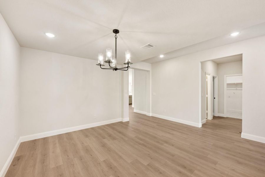 Empty dining room with light wood floors, white walls, and black chandelier with glass shades