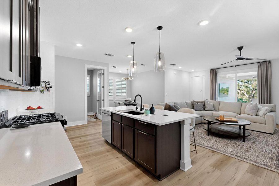 Kitchen featuring espresso cabinetry, a kitchen island with sink, decorative light fixtures, a breakfast bar area, and light wood-type flooring