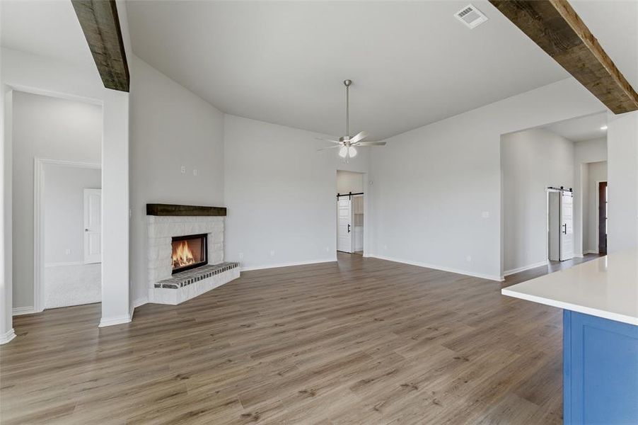 The spacious living area features light wood-style flooring, a white brick fireplace with a dark wood mantel, and a ceiling fan