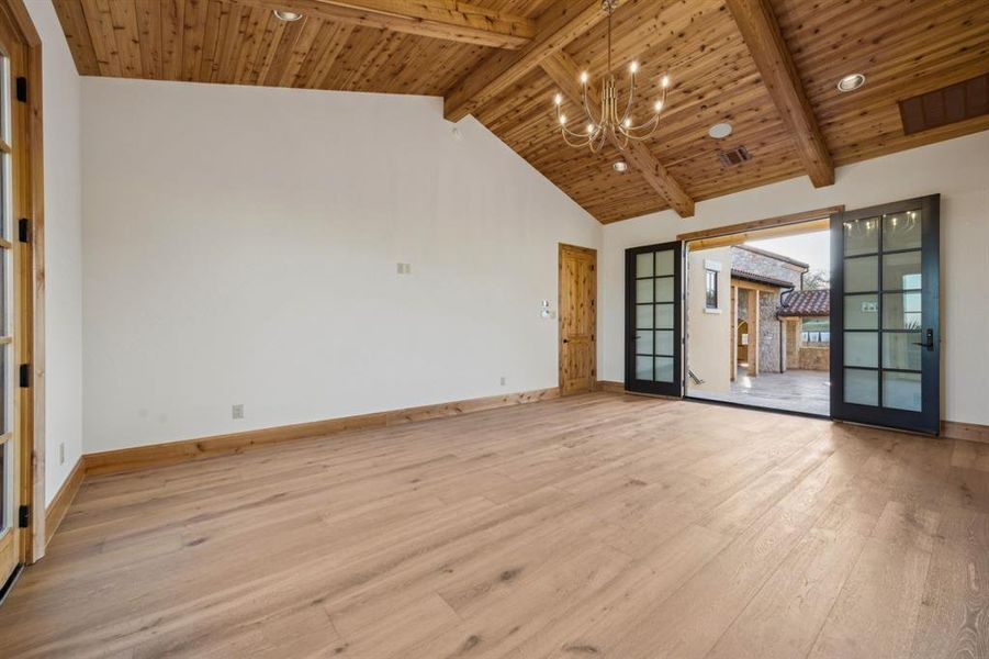 Empty room featuring french doors, hardwood / wood-style floors, a wooden ceiling with exposed beams, high vaulted ceiling, and a chandelier