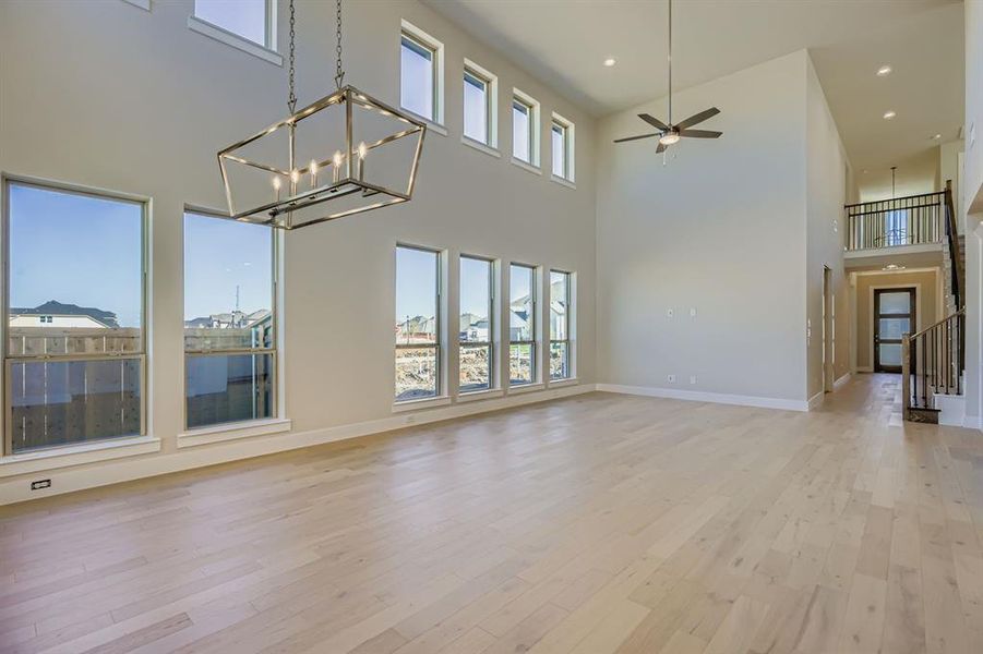 Unfurnished living room with light wood finished floors, ceiling fan, a towering ceiling, a chandelier, and recessed lighting