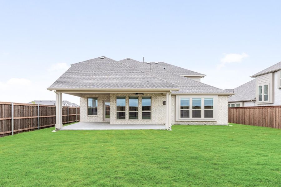 Rear exterior of brick home with covered patio, large windows, and fenced backyard lawn