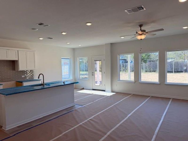 Kitchen with backsplash, white cabinetry, a kitchen island with sink, ceiling fan, and open floor plan Kitchen with backsplash, white cabinetry, a kitchen island with sink, ceiling fan, and open floor plan