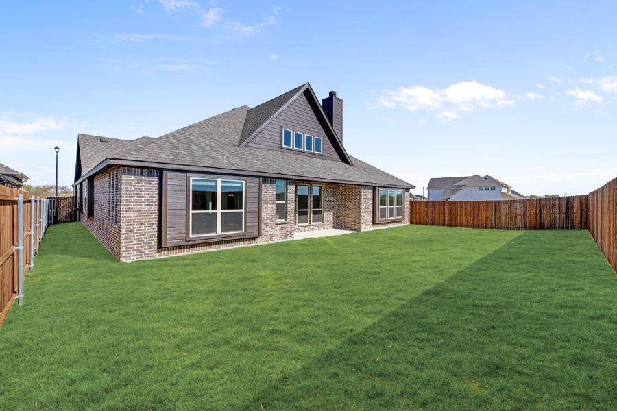 Rear view of brick home with dark siding, large windows, green lawn, and wood privacy fence Rear view of brick home with dark siding, large windows, green lawn, and wood privacy fence