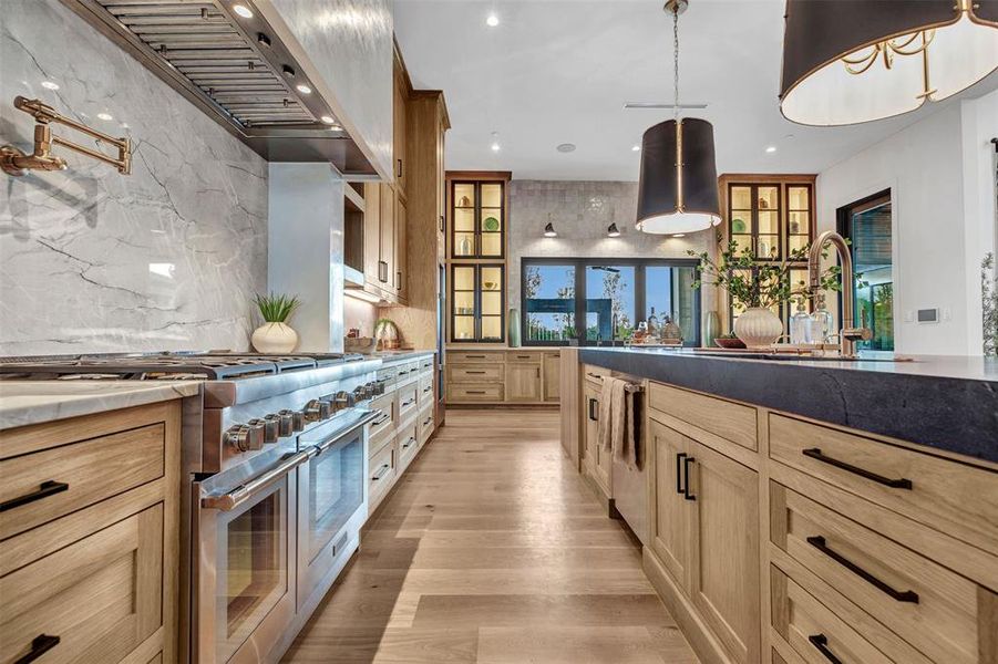 Kitchen with stainless steel appliances, pendant lighting, light wood-style floors, light brown cabinetry, and custom exhaust hood Kitchen with stainless steel appliances, pendant lighting, light wood-style floors, light brown cabinetry, and custom exhaust hood