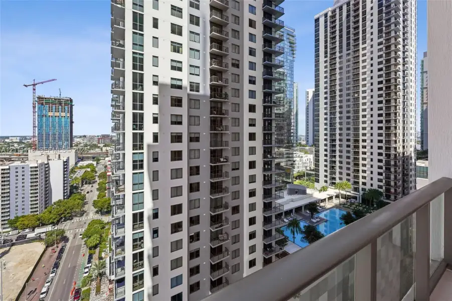 High-rise balcony featuring a metal-framed glass railing, oriented toward urban infrastructure and an outdoor swimming pool area