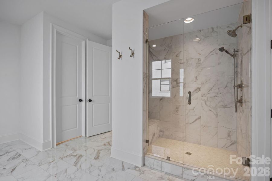 Floor to ceiling tile in custom shower with two showerheads, handheld wand, and bench seating
