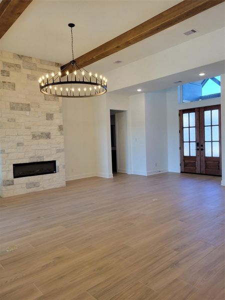 This spacious living area features a modern stone fireplace, elegant wood beams, and a stylish chandelier. The room is bright with natural light from large windows, and the wooden flooring adds warmth. The entryway boasts double doors, creating an inviting atmosphere. This spacious living area features a modern stone fireplace, elegant wood beams, and a stylish chandelier. The room is bright with natural light from large windows, and the wooden flooring adds warmth. The entryway boasts double doors, creating an inviting atmosphere.