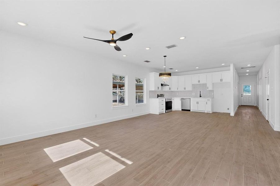 Unfurnished living room with recessed lighting, light wood-style flooring, a chandelier, and a ceiling fan